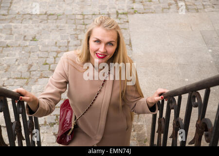 Giovane donna in cappotto sorrisi e passeggiate su per le scale Foto Stock