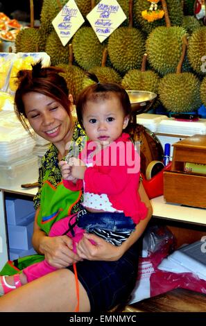 Bangkok, Thailandia: madre detiene a sua figlia in uno stand in o Tor Kor cibi freschi di mercato dove lei vende frutta Durian Foto Stock