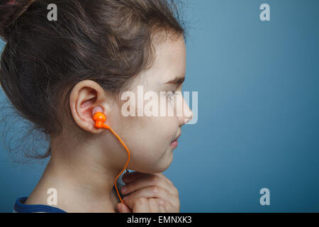 Una bambina di sette anni aspetto europeo brunette l'ascolto di musica con cuffie su uno sfondo grigio ventilatore di musica Foto Stock