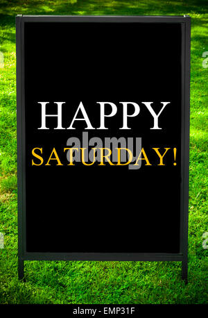 Felice sabato messaggio sul marciapiede di blackboard segno contro erba verde dello sfondo. Copia dello spazio disponibile. Concetto di immagine Foto Stock