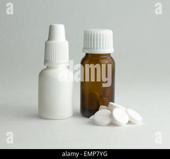 Piccola bottiglia di vetro scuro con un coperchio bianco e compresse. Foto Stock