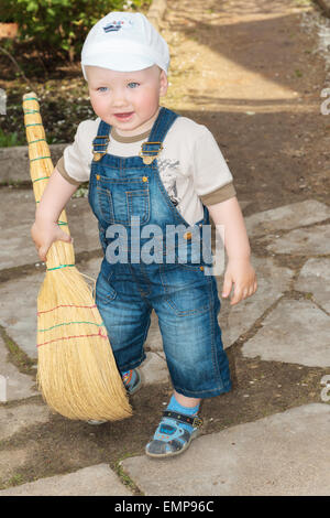 Il ragazzino in un cappello e un paio di jeans tuta con una scopa in mani. Foto Stock