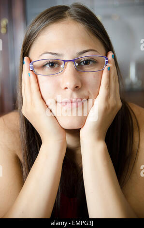 Giovani geeky ragazza con gli occhiali e le mani su una delle guance. Foto Stock