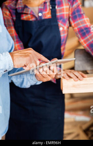 Carpenter con tavoletta digitale mentre guarda il collega Foto Stock