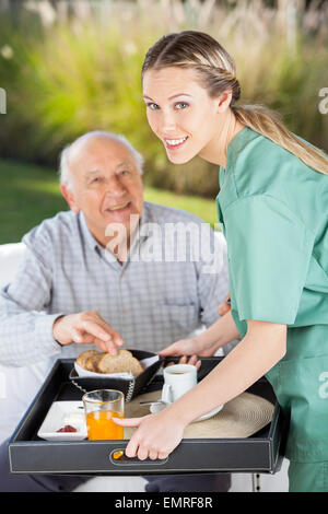Ritratto di donna sorridente infermiere che serve la prima colazione a senior uomo Foto Stock