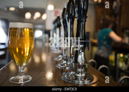 Una pinta di birra in un pub con un membro del personale dietro il bar Foto Stock