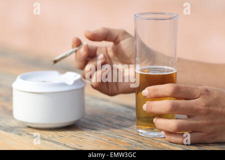 Donna mani tenendo una sigaretta fumare e bere alcolici in un bar di tabella Foto Stock