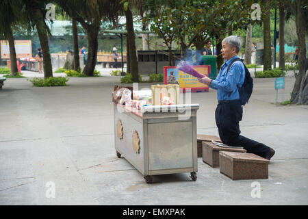 Un uomo con bastoncini di incenso è pregare in ginocchio, al Monastero Po Lin, a Hong Kong, Cina Foto Stock