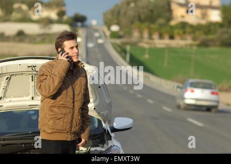 Uomo felice chiamando l'assistenza stradale per la sua ripartizione auto in una strada di campagna Foto Stock