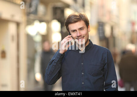 Vista frontale di un uomo felice chiamando al telefono a camminare sulla strada Foto Stock