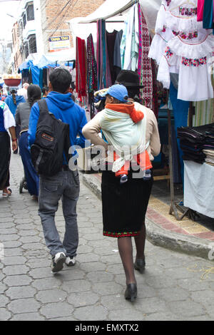 La donna che porta il bambino mentre lo shopping al mercato di Otavalo, Ecuador Foto Stock