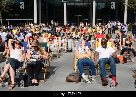 Le persone sedute a sdraio sul marciapiede durante la pausa pranzo in una giornata di sole a Londra Foto Stock
