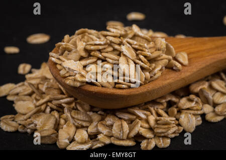 Fiocchi di avena su un cucchiaio di legno sul bordo scuro Foto Stock