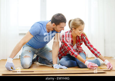 Coppia sorridente misurando il pavimento in legno Foto Stock