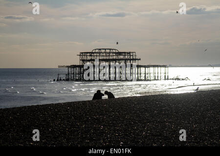 Un giovane sulla spiaggia di Brighton, con i resti del distrutto Molo Ovest in background Foto Stock