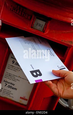 Persona pubblicando un Regno Unito voto postale busta scrutinio per l'elezione in un tradizionale britannico rosso scatola del montante Foto Stock