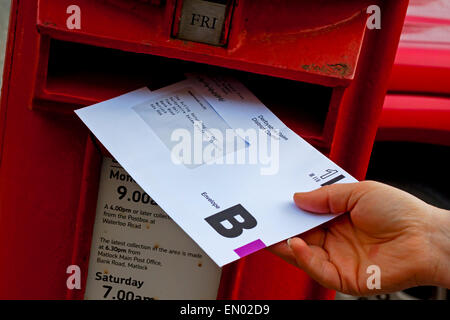 Persona pubblicando un Regno Unito voto postale busta scrutinio per l'elezione in un tradizionale britannico rosso scatola del montante Foto Stock