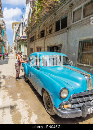 Un uomo afro-cubane pulisce la sua anni cinquanta turchese 4 porte automobile Pontiac fuori in Havana Vieja. Foto Stock