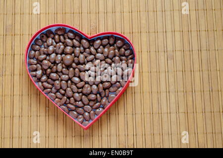 A forma di cuore scatola riempita con piccole sfere di cioccolatini sul tavolo di legno Foto Stock