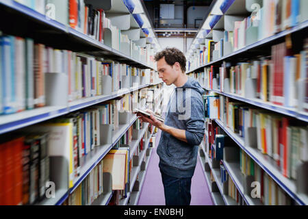 Giovane studente libro di lettura tra gli scaffali della biblioteca Foto Stock