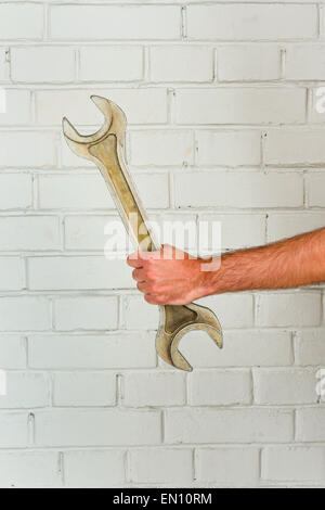 Mano d'uomo con chiave grande bianco contro un muro di mattoni Foto Stock