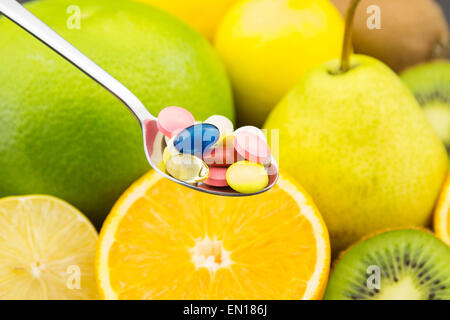 Cucchiaio colmo di pillole colorate sullo sfondo di frutta fresca Foto Stock