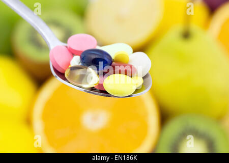 Cucchiaio colmo di pillole colorate contro lo sfondo della frutta succosa Foto Stock