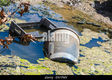 Garbage, scatole di plastica e bin tirato in un fiume con acqua contaminata Foto Stock