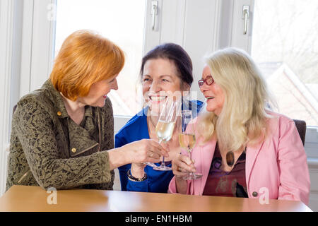 Tre felice Medioevo Mom migliori amici Tossing bicchieri di vino bianco e sorridente ogni altro mentre è seduto al tavolo di legno ho Foto Stock