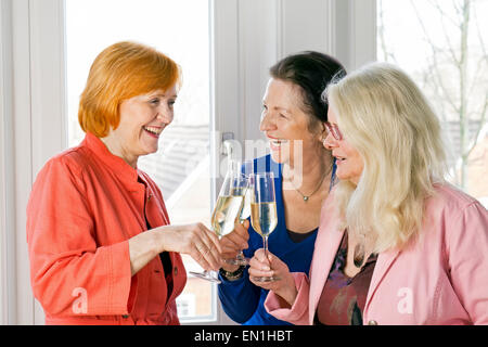 Close up. Tre felici donne adulte amici in abbigliamento alla moda nel lanciare bicchieri di vino bianco mentre rideva di qualcosa. Foto Stock