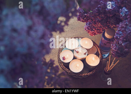 Piccole candele bianche in un cestello, olio da massaggio e essenza circondato da bellissimi viola lilla. Foto Stock