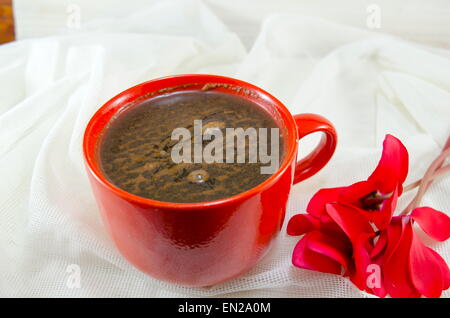 Red tazza di caffè decorato con schiuma e un fiore di una romantica tovaglia vintage Foto Stock