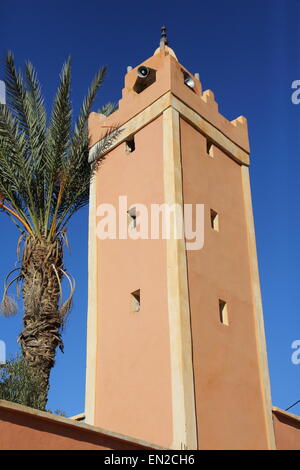 Un dipinto di rosso moschea in Alto Atlante in Marocco vicino Amizmiz insieme contro il cielo blu con un albero di palma vicino. Foto Stock