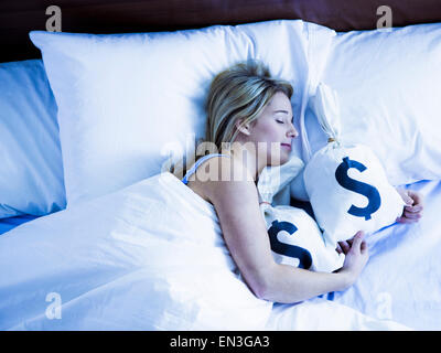 Giovane donna che dorme nel letto con sacchi di denaro Foto Stock