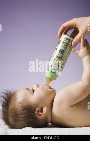 Baby di bere dalla bottiglia con valuta statunitense in esso Foto Stock