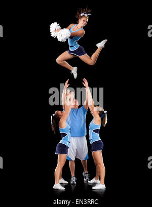 Studio shot di cheerleaders (16-17) di assistere amico durante il salto Foto Stock