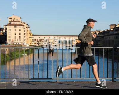 L'Italia, Firenze, uomo jogging passato il Ponte Vecchio oltre il fiume Arno Foto Stock