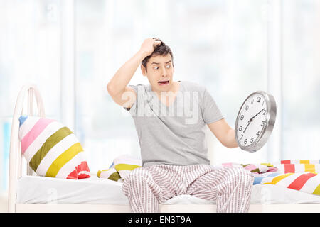 Scioccato l uomo in pigiama guardando al tempo di incredulità e seduta sul suo letto a casa Foto Stock