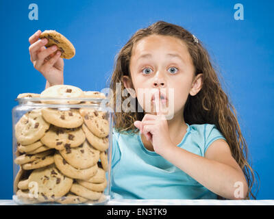 Ragazza tenendo Chocolate Chip Cookie da jar e hushing Foto Stock