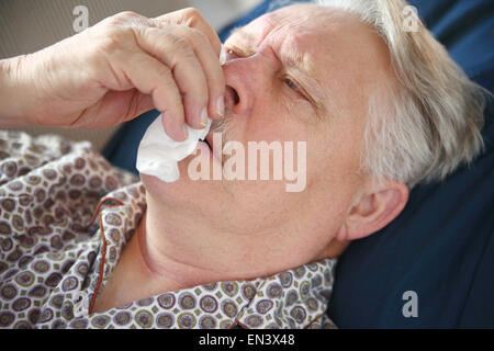 Malati senior uomo giace sul divano e tende al suo naso che cola. Foto Stock