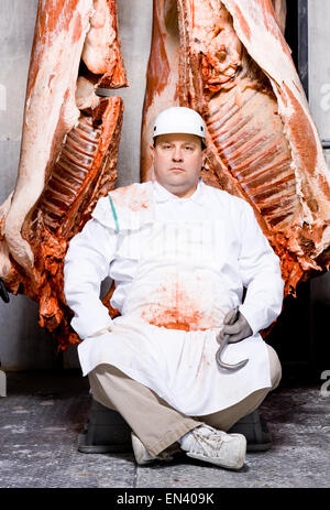 Butcher seduto con la carcassa e gancio di carne Foto Stock