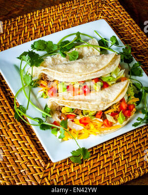 Una piastra di Tacos con lattuga, pomodoro,l'avocado e coriandolo su un caricabatteria di bambù Foto Stock