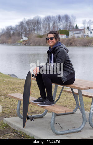 Calma donna seduta sul tavolo da picnic su un parco con longboard Foto Stock