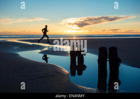 Uomo che corre sulla spiaggia al tramonto a Sandsend, North Yorkshire, Regno Unito. Foto Stock