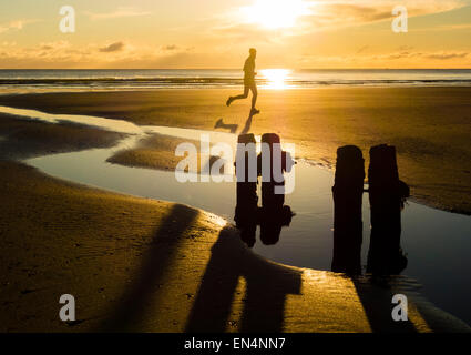 Uomo che corre sulla spiaggia al tramonto a Sandsend, North Yorkshire, Regno Unito. Foto Stock