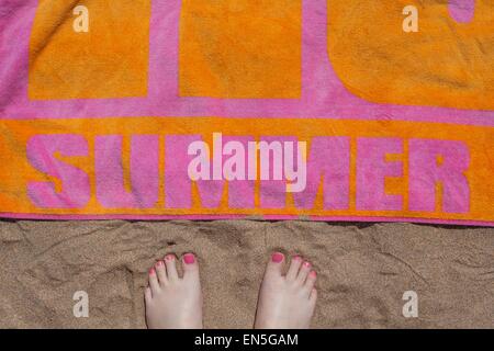 Piedi vista di piedi vicino a una spiaggia colorata asciugamano sulla sabbia Foto Stock