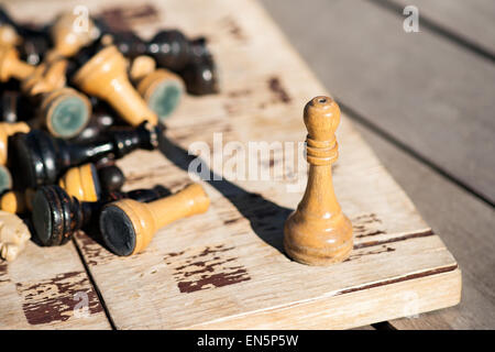Vecchio e appassiti Scacchi in legno re su un vecchio e appassiti scacchiera. Altri pezzi di scacchi di nero e il colore bianco laici in pila Foto Stock