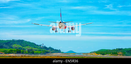 Twin-motore, aereo commerciale in arrivo per un atterraggio in un aeroporto in un ambiente tropicale, a sud-est del paese asiatico. Un luminoso cielo blu Foto Stock