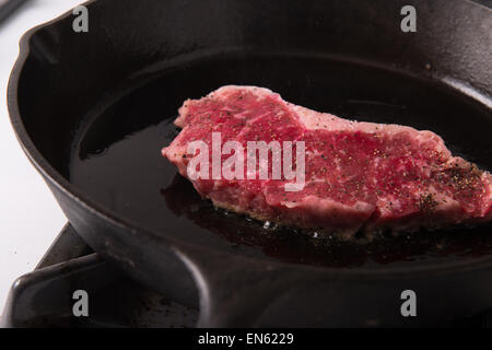 Serie: Striscia di grigliatura Bistecca di lombo in ghisa Padella: bistecca in padella con sale e pepe e olio di oliva Foto Stock