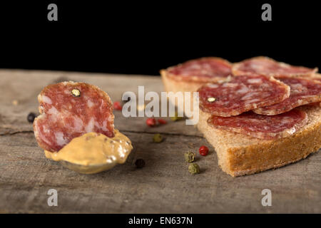 Fetta di salame in salsa di senape con semi e un sandwich di salame con sfondo nero Foto Stock